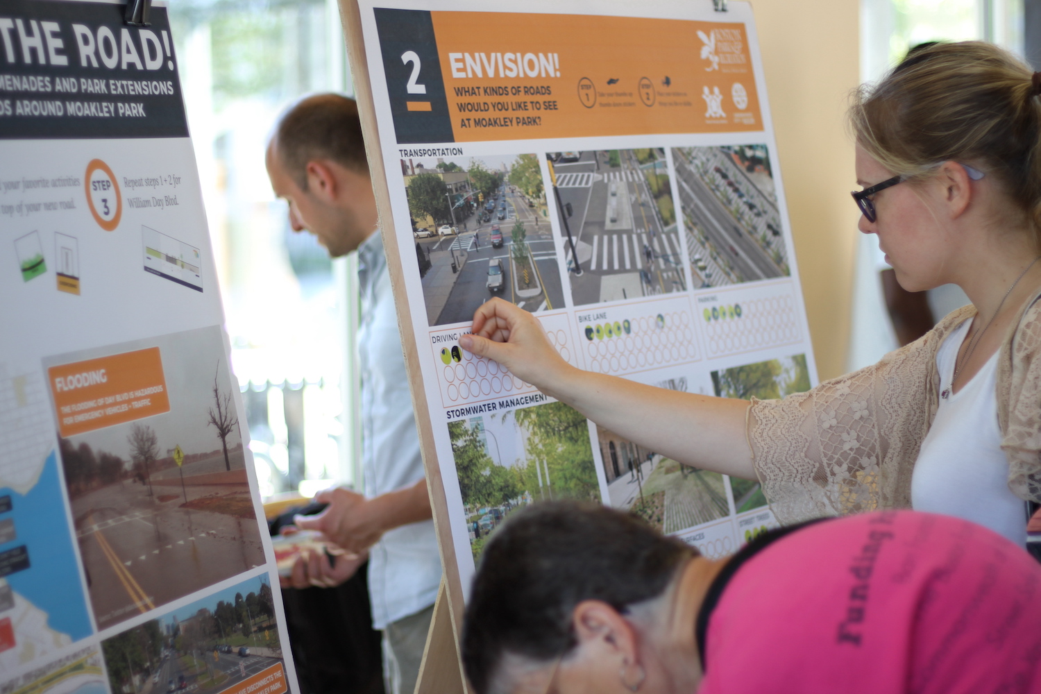 One person puts sticky dots on an engagement panel from Moakley Park