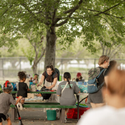 A group of people engaged in various activities under a tree in Moakley Park