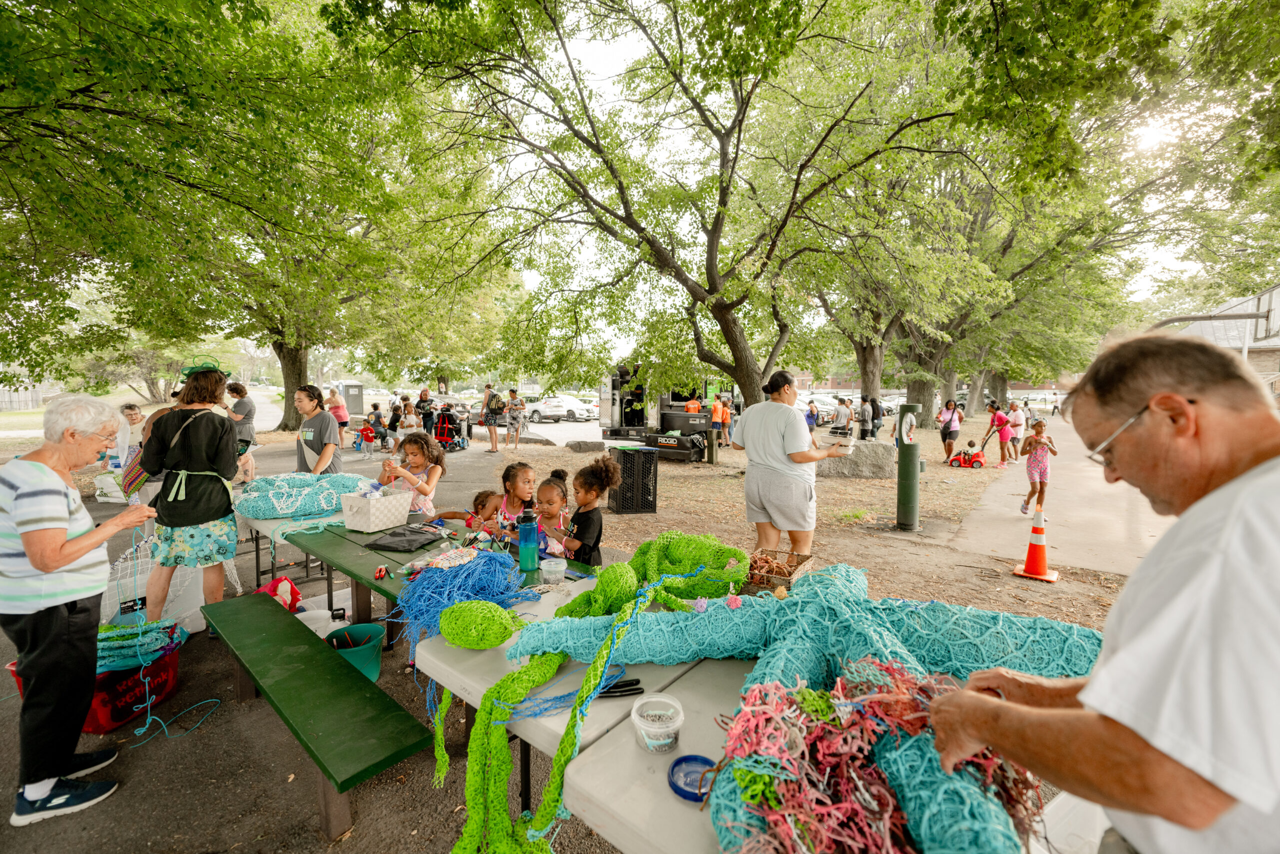 Multiple generations of people working on a table covered in colorful sea creatures made from recycled materials.