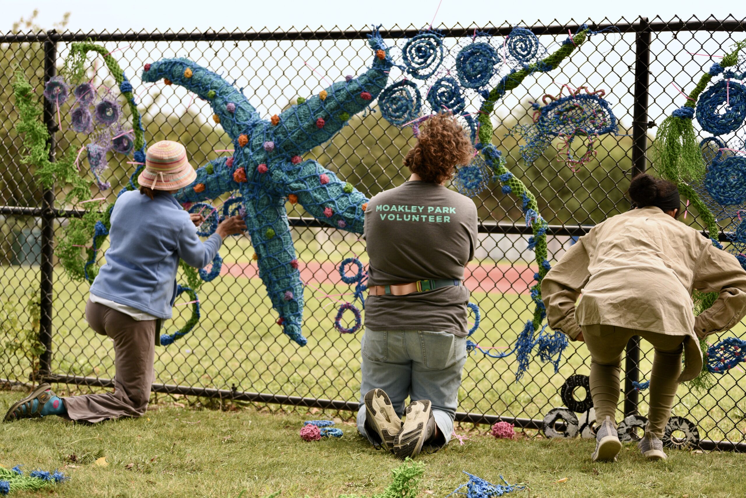 hree volunteers attach pieces of the sculpture onto a fence.